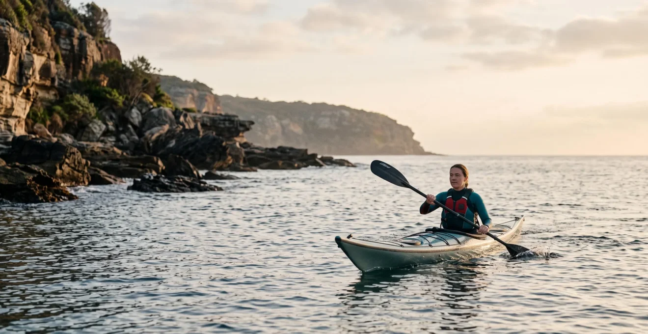 Kayakiste solitaire pagayant calmement le long d'une côte rocheuse au lever du jour, illustrant les débuts sécurisés du kayak de mer