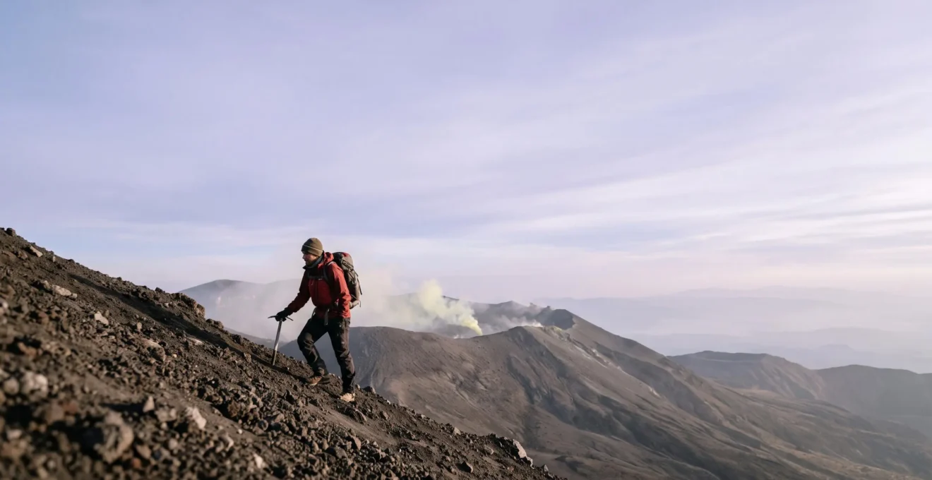 Silhouette d'un alpiniste gravissant l'arête d'un volcan au lever du jour, entoure de fumerolles