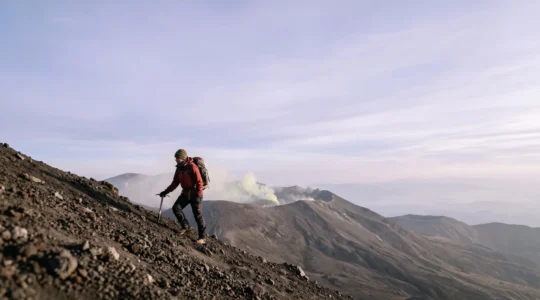 Silhouette d'un alpiniste gravissant l'arête d'un volcan au lever du jour, entoure de fumerolles