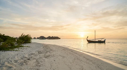 Lagon turquoise des Maldives au coucher du soleil avec un bateau traditionnel dhoni voguant vers une villa sur pilotis