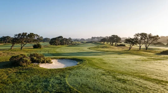 Fairway sinueux d'un parcours de golf mythique baigne par la lumiere doree du soir, sans aucun joueur visible
