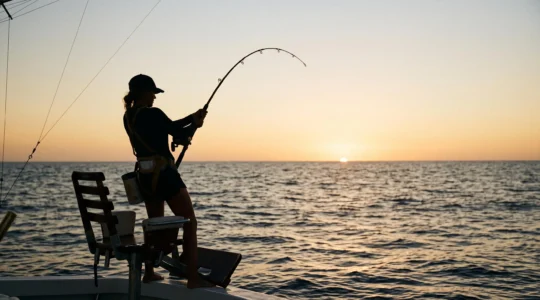 Pêcheur en plein combat avec une grosse prise au lever du soleil sur un bateau de pêche au gros en haute mer