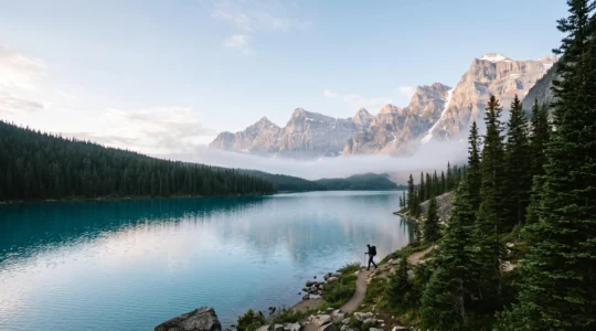Vue panoramique d'un lac alpin entouré de sommets enneigés avec un randonneur au petit matin, symbolisant les vacances actives en Haute-Savoie toute l'année